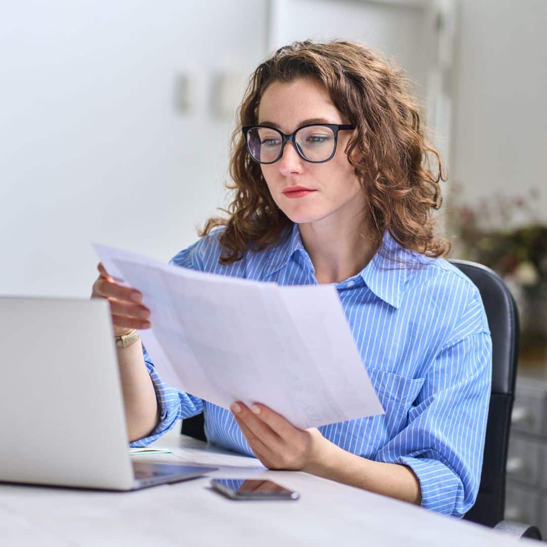 A bookkeeper reviewing reports and working on her laptop.